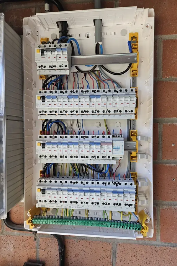 Open verdeelkast tegen een bakstenen muur, met rijen automaten en netjes gebundelde draden
