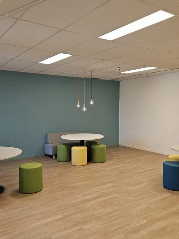 Kantine met ronde tafels en poefs, met hanglampen boven de tafels en ledpanelen in het plafond