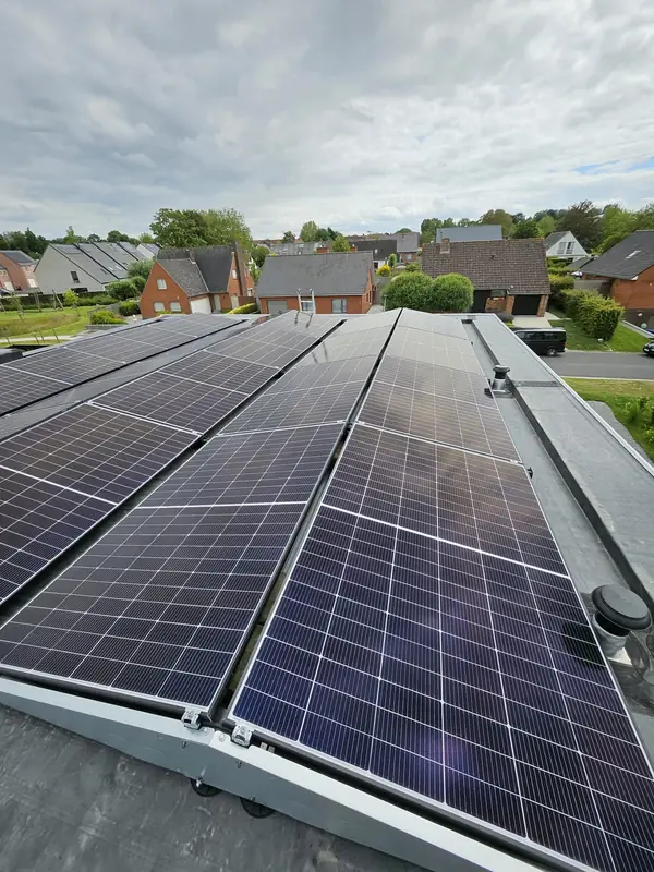 Lange rijen zonnepanelen op een plat dak, met een woonwijk op de achtergrond